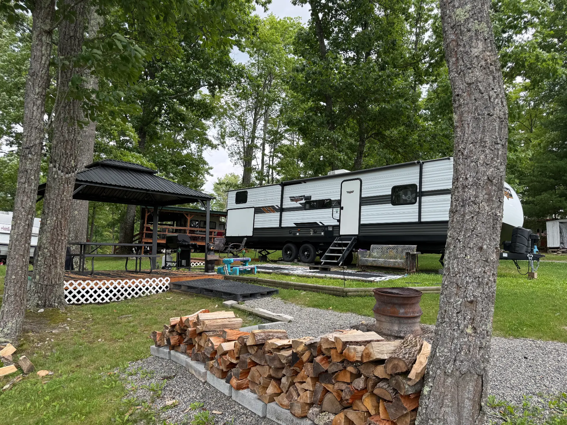 Travel trailer beside a covered gazebo deck with a stack of firewood