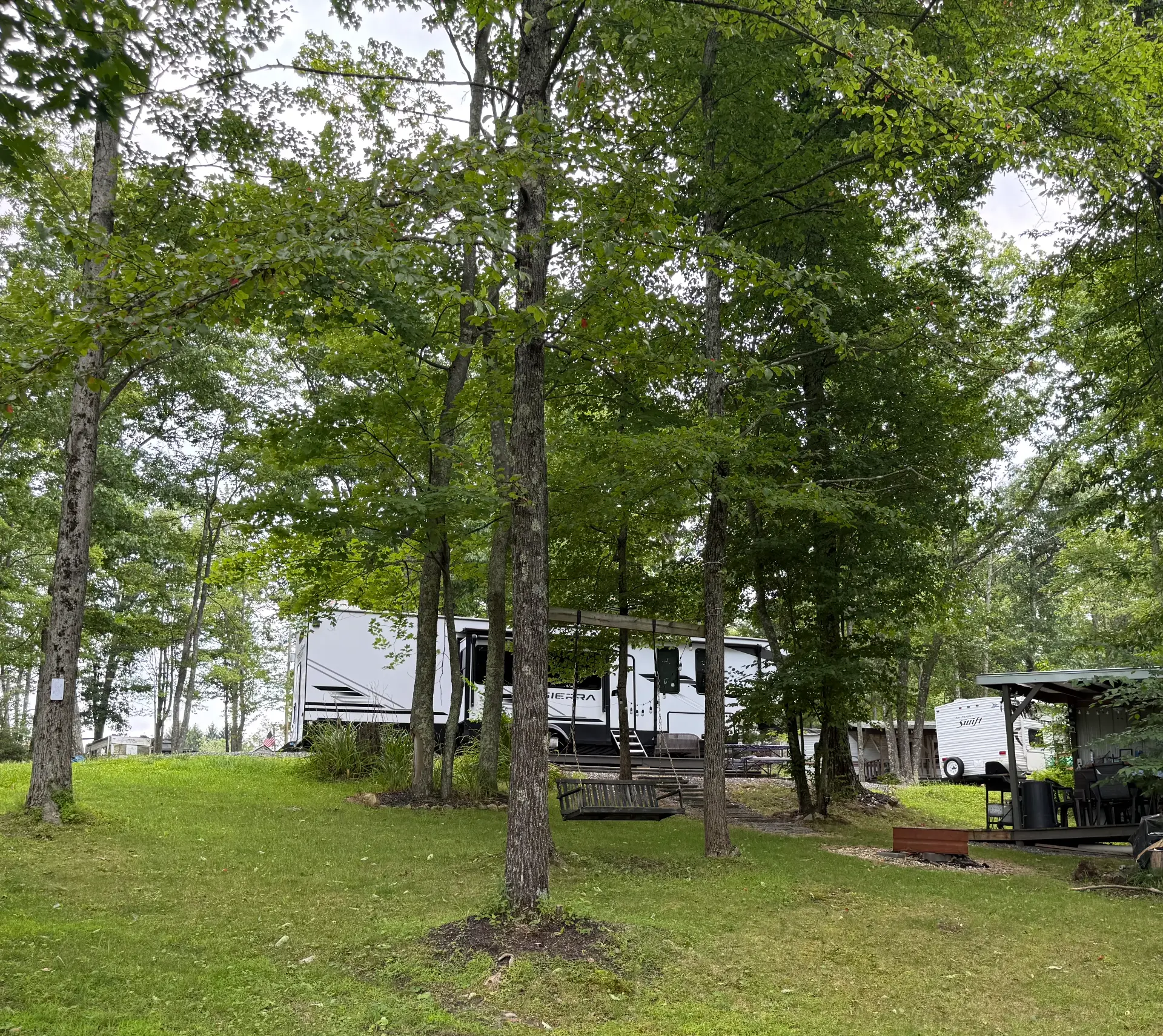Camper parked among tall shade trees with a porch swing in the foreground