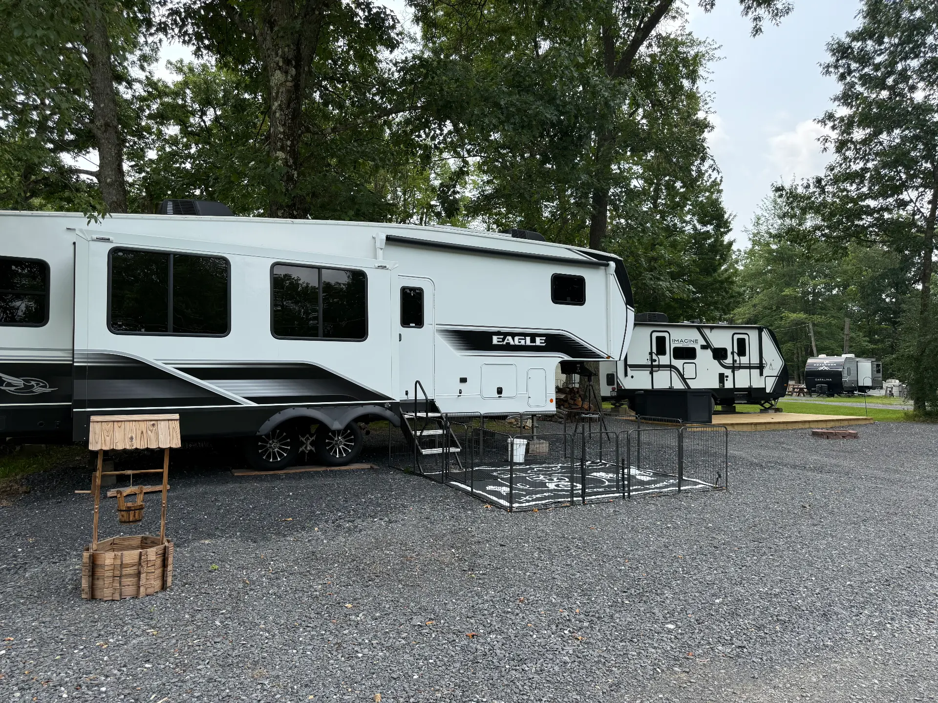 Large fifth-wheel camper on a gravel full hook-up site with a wooden deck