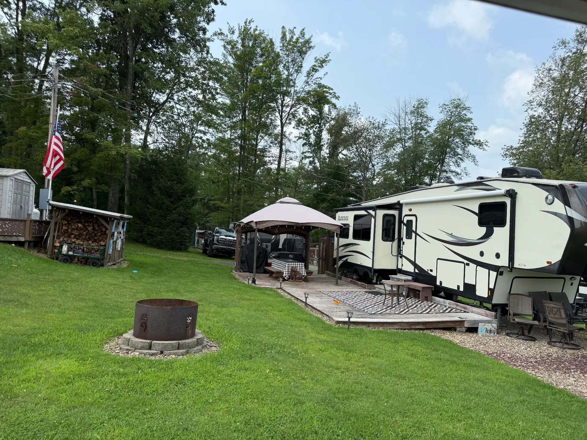 Fifth-wheel camper on a grassy site with a fire ring and American flag