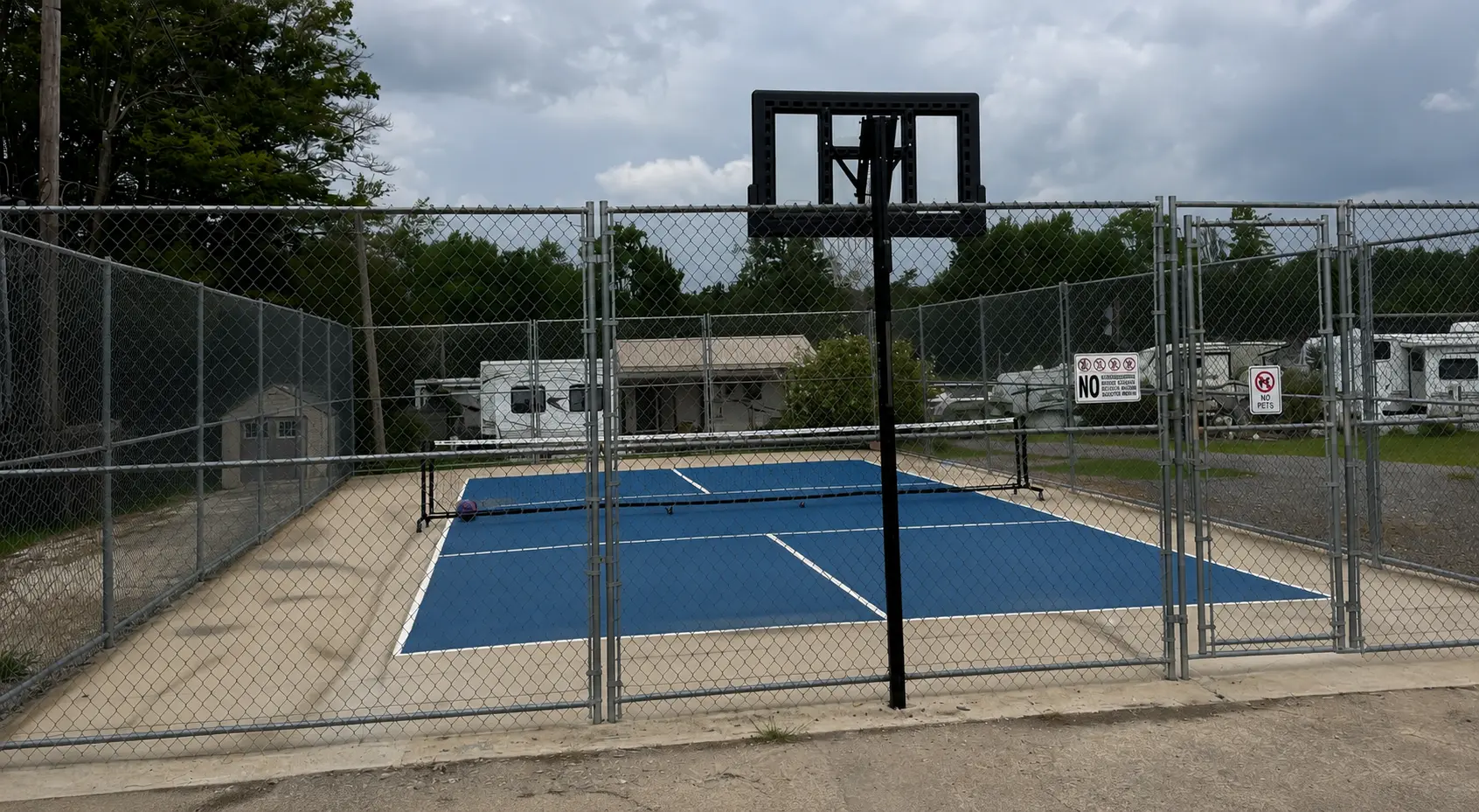 Fenced pickleball court with a basketball hoop